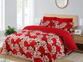 Red floral quilt set on a bed in a bedroom with a window and lamp.
